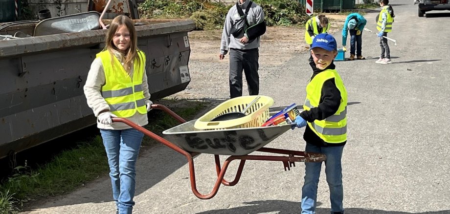 Man sieht 2 Kinder die eine Schubkarre tragen