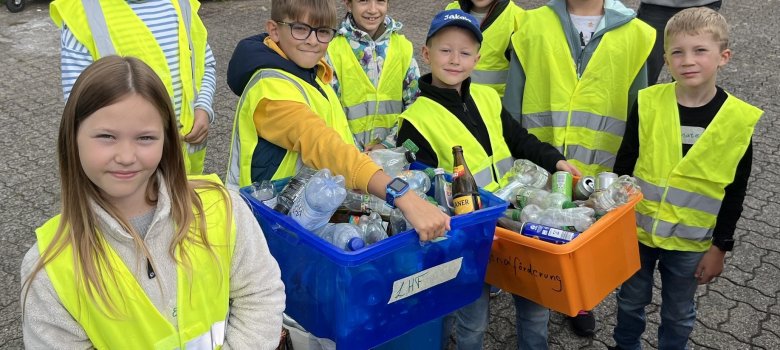 Man sieht Kinder in gelben Warnwesten. Zwei Kinder halten Kisten mit gesammelten Plastikflaschen/Müll hoch